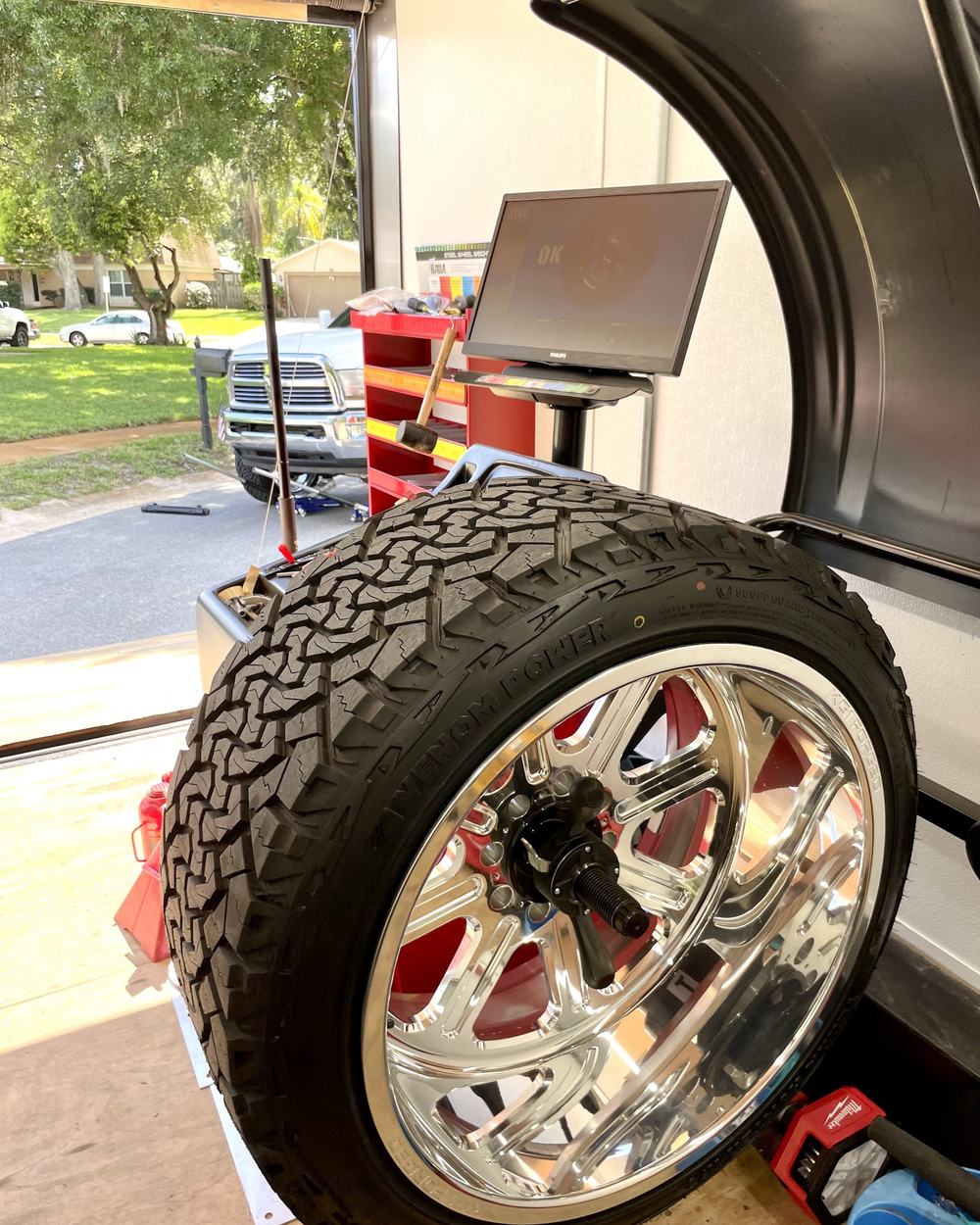 A large polished wheel and all-terrain tire mounted on the computerized wheel balancer in the trailer